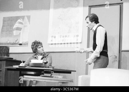 Theater evening in the Airport, Theater, 26-11-1977 Whizgle News, Dutch Desk, The Netherlands, 1950-2000 A woman sits at a desk with a typewriter, looking intently at a man who stands nearby, gesturing as he speaks. The room features a map on the wall and a sailboat poster, adding context to their conversation, which seems tense and important. Stock Photo