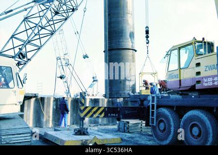 Installing access shaft PWN Vijfhuizen, Vijfhuizen, 18-11-1998 Whizgle News, Dutch Desk, The Netherlands, 1950-2000 A construction site featuring heavy machinery, where workers are engaged in installing a large cylindrical structure, assisted by cranes and lifting equipment. The scene highlights the collaboration and effort involved in large-scale infrastructure projects. Stock Photo