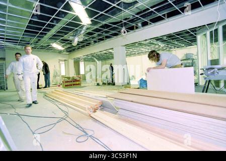 Rabobank renovation, IJmuiden, The Netherlands, 27-11-2000 Whizgle News, Dutch Desk, The Netherlands, 1950-2000 A team of workers is engaged in a construction project inside a building. One person is focused on installing a panel, while two others walk past structural materials and tools. The space appears to be in the midst of renovations, featuring exposed materials and an unfinished ceiling. Stock Photo
