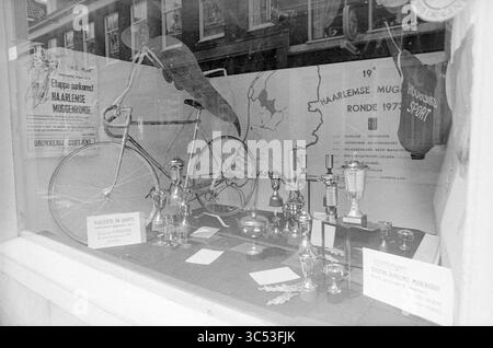 Shop window with attributes of the Mosquito Round decorated by Mr. J. van Riessen, one of the organizers, in the building at Koningstraat 16, Exterieur, Haarlem, Koningstraat, The Netherlands, 13-06-1973 Whizgle News, Dutch Desk, The Netherlands, 1950-2000 A vintage bicycle is displayed alongside an array of trophies and awards, highlighting a historical cycling event. A map is featured in the background, marking locations relevant to the event, while a sports jersey adds to the nostalgic atmosphere. Stock Photo