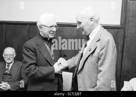 Papal Award Mr. A.P. Goosen, Awards, 26-01-1981 Whizgle News, Dutch Desk, The Netherlands, 1950-2000 Two men are engaged in a warm handshake, sharing a moment of connection and camaraderie. One man, dressed in clerical attire, smiles as he interacts with a man in a suit. In the background, an older gentleman observes the exchange, adding to the atmosphere of camaraderie. Stock Photo