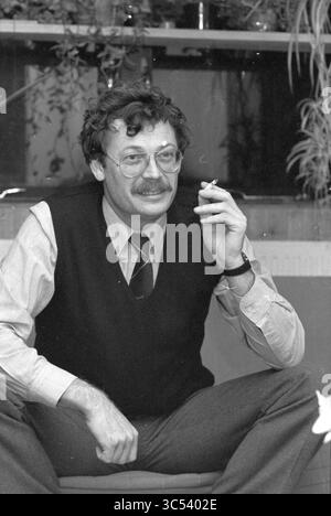 Mr Joost Brouw councilor Zwaanshoek, Persons, Zwaanshoek, 28-11-1983 Whizgle News, Dutch Desk, The Netherlands, 1950-2000 A man sits casually with a slight smile, holding a cigarette, dressed in a vest and collared shirt, exuding a relaxed yet thoughtful demeanor. He's surrounded by greenery in a cozy setting. Stock Photo