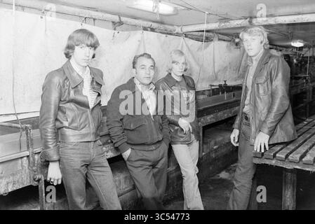 4 herring fishermen on boat IJm. 36, Herring fishing, herring, 21-07-1978 Whizgle News, Dutch Desk, The Netherlands, 1950-2000 A group of four individuals stands together in a dimly lit, industrial space. Two young men and a young woman are dressed in stylish leather jackets, while an older man in a more formal jacket poses confidently among them. The setting has a utilitarian feel, with metal surfaces and a workbench creating a backdrop for their casual yet striking presence. Stock Photo