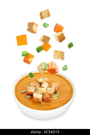 Croutons, green onion and pumpkin cubes falling into bowl of soup against white background Stock Photo