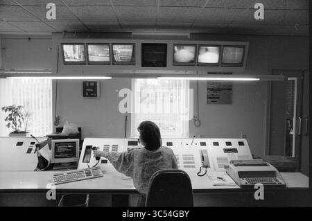 Velsen Police Control Room, Velsen, 02-05-1991 Whizgle News, Dutch Desk, The Netherlands, 1950-2000 A person sits at a control desk surrounded by multiple screens displaying surveillance footage. The workspace features various monitors, a computer, and a telephone, with a large window letting in natural light. The atmosphere conveys a sense of focus and monitoring. Stock Photo