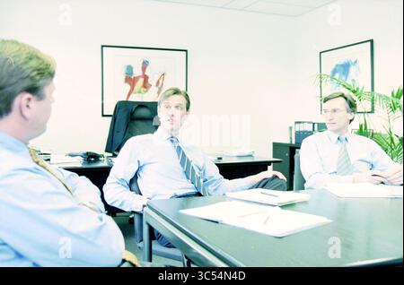 Meeting, Fluor Daniel, Haarlem, The Netherlands, 07-04-1999 Whizgle News, Dutch Desk, The Netherlands, 1950-2000 Three professionals engage in a discussion around a conference table in an office setting, with documents and stationery scattered around. The atmosphere appears focused and collaborative, highlighted by vibrant artwork on the walls. Stock Photo