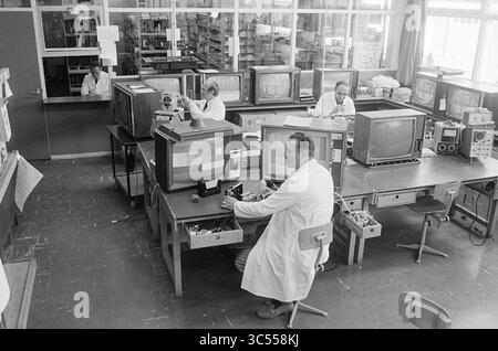 Award ceremony Technical Service., Award ceremony, 10-06-1970 Whizgle News, Dutch Desk, The Netherlands, 1950-2000 A group of professionals in lab coats is working in a technology workshop, focusing on various television sets and electronic equipment. The room is filled with desks cluttered with tools and components, highlighting a busy environment dedicated to repair and innovation. Stock Photo