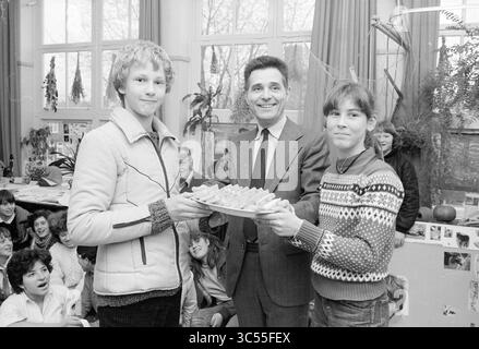 Award ceremony Huishoudschool IJmuiden + tile tableau, Schools, IJmuiden, The Netherlands, 25-03-1981 Whizgle News, Dutch Desk, The Netherlands, 1950-2000 Two young students proudly hold a tray of treats, smiling as they stand next to a well-dressed man who beams with delight. A classroom filled with amused peers in the background captures the joyful atmosphere of the moment. Stock Photo