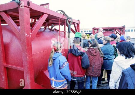 Students Kruisbergschool near Halliburton, IJmuiden, IJmuiden, The Netherlands, 16-12-1996 Whizgle News, Dutch Desk, The Netherlands, 1950-2000 A group of people gathers around a large red container, seemingly engaged in a discussion. Some individuals are wearing colorful jackets, while others showcase varied attire, indicating a diverse group. The setting appears to be industrial, with visible equipment and structures nearby. Stock Photo