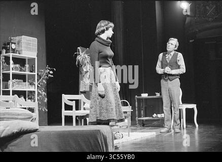 Theater Landjuweel Rotterdam, Theater, 03-06-1976 Whizgle News, Dutch Desk, The Netherlands, 1950-2000 A woman in a stylish outfit stands attentively as a man, dressed in vintage attire, engages her in conversation. The setting features a simple living room with a table and plants, suggesting a domestic scene filled with tension and emotion. Stock Photo