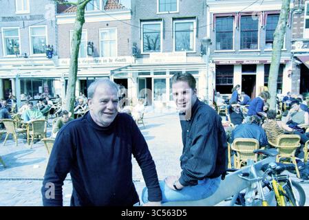 Luc + Julian Wildschut, café on the Botermarkt, Haarlem, Botermarkt, The Netherlands, 22-04-1998 Whizgle News, Dutch Desk, The Netherlands, 1950-2000 Two men sit outdoors in a lively café atmosphere, with tables and people around them enjoying their time. The scene captures a blend of relaxed conversation and social interaction, set in a charming urban environment. One man, casually dressed in a dark sweater, smiles at the camera, while the other, in a black shirt, leans slightly forward, appearing engaged and friendly. Stock Photo