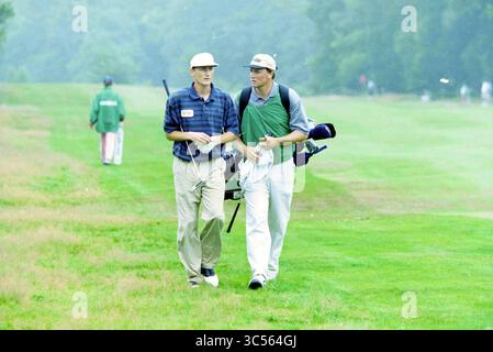 Golf, Heineken Open, Hilversum, Hilversum, 29-07-1995 Whizgle News, Dutch Desk, The Netherlands, 1950-2000 Two golfers stroll down a lush fairway, casually chatting as they carry their equipment. One golfer is dressed in a plaid shirt and cap, while the other wears a green vest over a collared shirt, both embodying a relaxed day on the course. Stock Photo