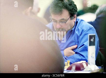 CCT-Brain, Wijk aan Zee, Wijk aan Zee, 16-01-2002 Whizgle News, Dutch Desk, The Netherlands, 1950-2000 A focused man in a blue shirt thoughtfully contemplates his next move in a chess game, with pieces positioned in front of him. His arms are crossed as he concentrates, surrounded by the soft blur of others engaged in the same intellectual challenge. Stock Photo