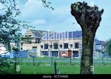 New construction, Hoofdstraat, Santpoort, Santpoort-Noord, Hoofdstraat, 06-03-1995 Whizgle News, Dutch Desk, The Netherlands, 1950-2000 A partially constructed building stands behind a recently cut tree stump, surrounded by an open field. The structure features a modern design with a solar panel roof, and nearby, construction materials are visible. Sparse trees dot the landscape, emphasizing the contrast between nature and development. Stock Photo