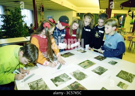Most beautiful photo in the newspaper, Haarlem, The Netherlands, 24-11-1998 Whizgle News, Dutch Desk, The Netherlands, 1950-2000 A group of children is gathered around a large table, carefully examining pictures laid out before them. Some are writing notes, while others seem engaged in discussion, showcasing curiosity and collaboration in their activity. Various artworks or photos spread across the table add a creative atmosphere to the scene. Stock Photo