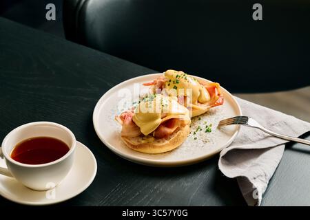 Gourmet eggs benedict with creamy hollandaise sauce, crispy bacon on english muffin served with fresh coffee. Perfect brunch dish at fine cafe. Stock Photo