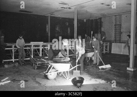 Activities PEN society, Society, Activities, 15-04-1970 Whizgle News, Dutch Desk, The Netherlands, 1950-2000 A group of workers is shown actively engaging in construction or renovation tasks, with wheelbarrows and tools scattered around. They appear to be focused on their work, collaborating to transform the space, which features wooden structures and a spacious, industrial atmosphere. Stock Photo