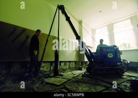 Activities Fabriciusstraat, Haarlem, Fabriciusstraat, The Netherlands, 12-07-2000 Whizgle News, Dutch Desk, The Netherlands, 1950-2000 Two workers are engaged in a construction project, using a heavy drilling machine in an interior space. One worker operates the machinery while the other stands nearby, ensuring safety and monitoring the progress as they remove materials from the wall. The setting appears to be a renovation site, with exposed ground and unfinished walls. Stock Photo