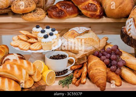 Variety of baked goods including croissants, bread, cupcakes with coffee grapes on display in bakery. Stock Photo