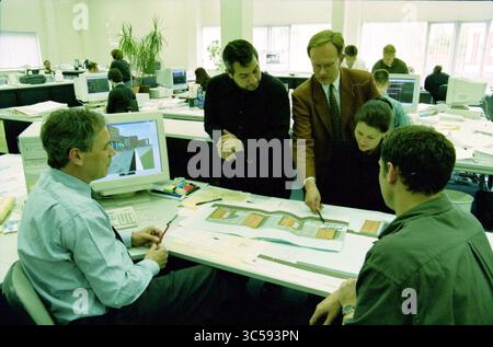 Pieters, Haarlem, The Netherlands, 30-04-2000 Whizgle News, Dutch Desk, The Netherlands, 1950-2000 A group of professionals engages in a collaborative discussion over architectural plans at an office workspace, with a computer displaying design software visibly in the background. Stock Photo