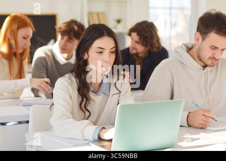 Students group working and study at laptop online at desk in college class, trainee interns sitting  Stock Photo