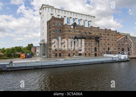 The historic Lassie building in Wormer, Netherlands, seen from the water with a docked cargo ship, showcases industrial heritage. Stock Photo