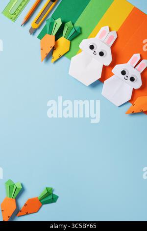 Frame made of paper crafting tools: craft knife, ruler, pencil, and colored paper. Origami rabbits and carrots. DIY concept, needlework. Flatlay, copy Stock Photo