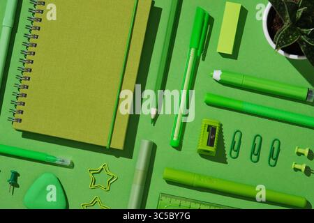 Close-up flat lay of assorted green office supplies on vibrant background, featuring spiral notebook, pens, pencil, sharpener, sticky notes, eraser, p Stock Photo