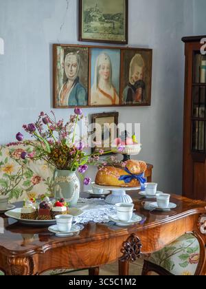 Easter-themed tea setting in a historical room with wooden furniture, floral upholstery, vintage paintings, and traditional Czech Easter lamb cake dec Stock Photo