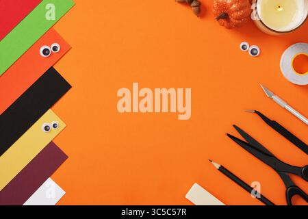 Supplies for paper crafts in Halloween colors. Pencil, eraser, knife, scissors, tape and colored pieces of paper. Stock Photo