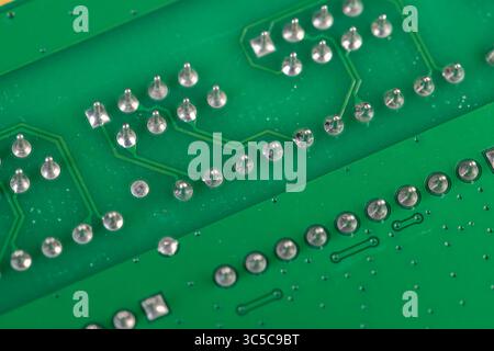 a green electronic circuit board with a large number of contacts, a simple green printed circuit board with an electronic circuit with soldered elemen Stock Photo