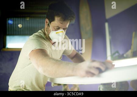 Craft, surfboard and polish with man in workshop for manufacturing, sports equipment and craftsman. Entrepreneur, maintenance and repair with person Stock Photo