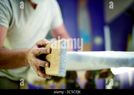 Man, hands and sanding surfboard in workshop for craft, inspection or quality control. Hobby, surfer or tools in studio for maintenance, equipment Stock Photo