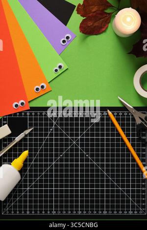 Supplies for Halloween-themed paper crafts. Pencil, glue, eraser, knife, scissors, and colored paper. Stock Photo