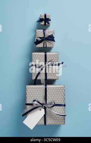 Four gift boxes of different sizes are lined up on a pastel blue background. Each gift is decorated with dark blue and silver satin ribbons. Stock Photo