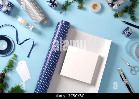 Unpacked box lies on wrapping paper. Around it are ribbon, scissors, tape, spruce twigs, and small wrapped gifts. Preparing for the holidays. Stock Photo