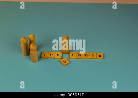 Wooden figures and the word "insurance" are arranged on a teal background, creating a visual representation of the concept. Stock Photo