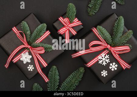 Three gift boxes with christmas tree branches and snowflakes on black background. Stock Photo