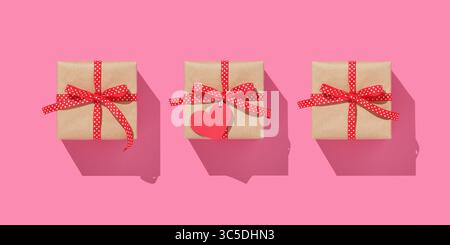 Three brown craft gift boxes with red ribbons on pink background. Heart-shaped label Stock Photo