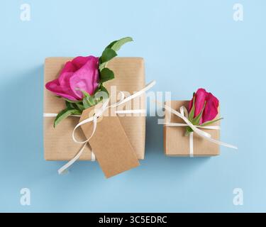 Two brown gift boxes with rosehip flowers and white ribbon on blue background. Stock Photo
