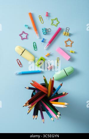 Stationery background with colored pencils in a cup, felt-tip pens, paper clips, clipboards, paper clips, sticky notes and push pins. Light blue back Stock Photo