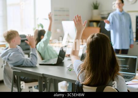 Group of Teenagers Raising Hands While Attending Lesson in Classroom Setting Stock Photo