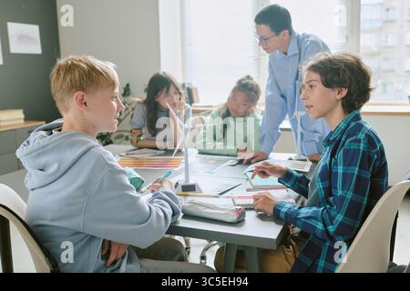 Diverse Group of Teenagers Collaborating on School Project with Teacher Assisting Stock Photo