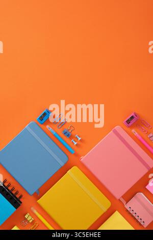 Banner with blue, yellow and pink notepads and colored office supplies on a bright orange background. Copyspace. Stock Photo