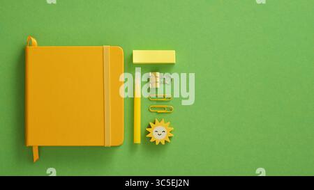 Closed yellow notepad with stationery felt-tip pen, paper clips, pins, stickers on a green background. Space for your text. Stock Photo
