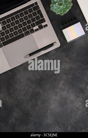 Neat workspace with laptop, pen, stickers and succulent plant on a dark textured background. Copy space. Stock Photo