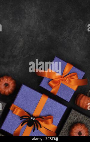 Halloween gifts with purple wrapping paper, orange ribbons, black spider, and mini pumpkins on a dark background. Copyspace. Stock Photo
