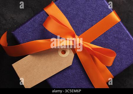 Halloween gift wrapped in purple paper with orange ribbon and rectangular blank tag. A place for your text Stock Photo