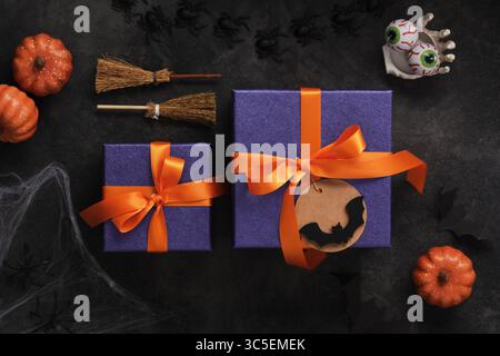 Purple Halloween gift boxes with orange ribbons and a blank label with a bat silhouette, broomstick, pumpkins and spooky decorations Stock Photo