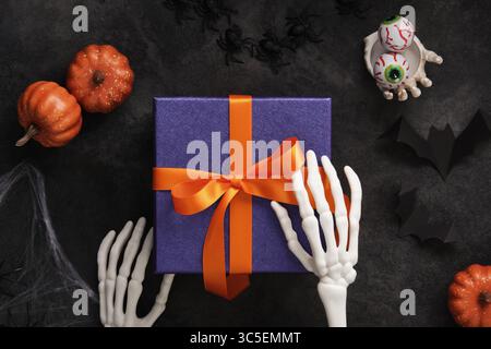 Purple Halloween gift boxes with orange ribbons with skeleton hands, broomstick, pumpkins and spooky decorations Stock Photo
